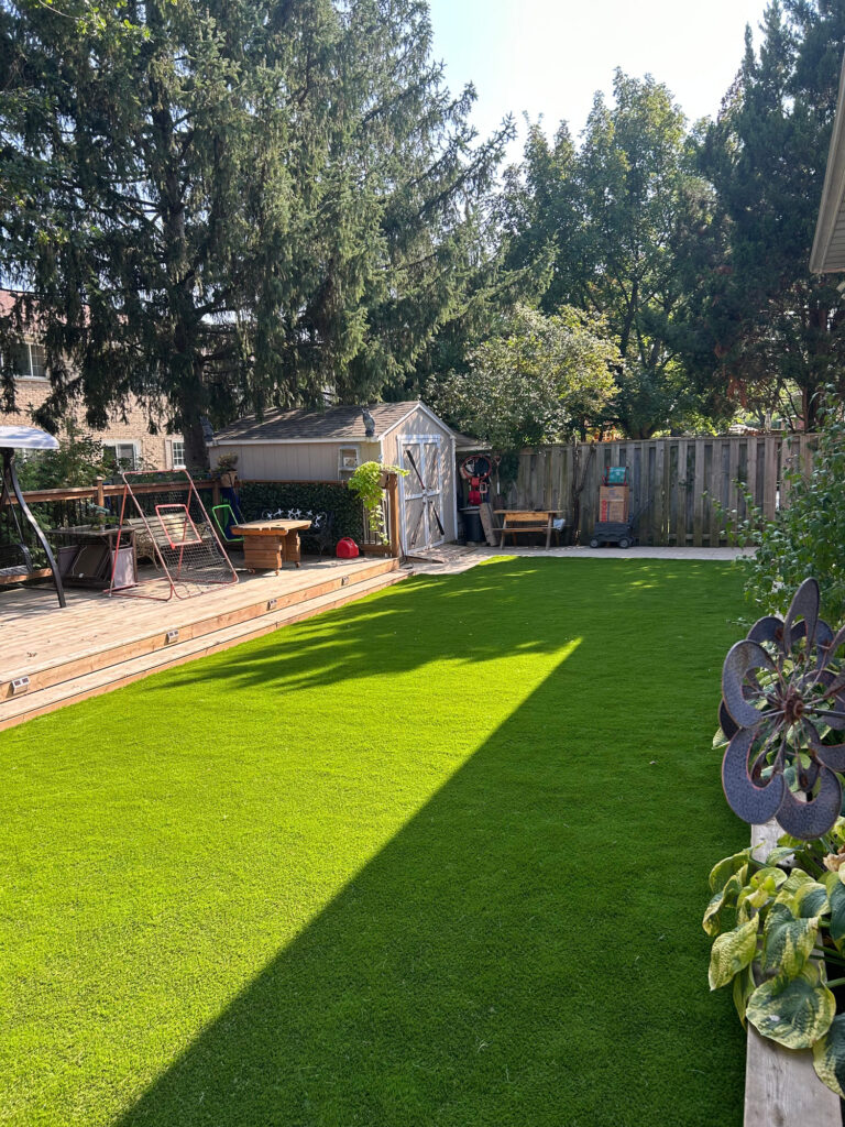 A long backyard lawn of artificial turf in sunlight