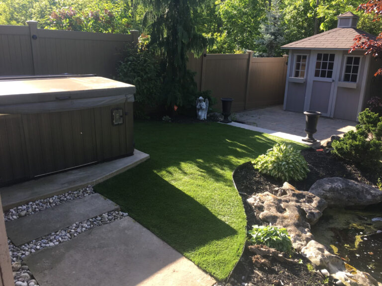 A dry creek bed of river stone winding between turf and a shed