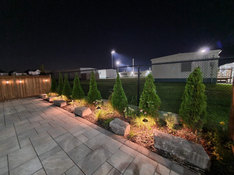 Boulders and evergreens lit at night beside a patio