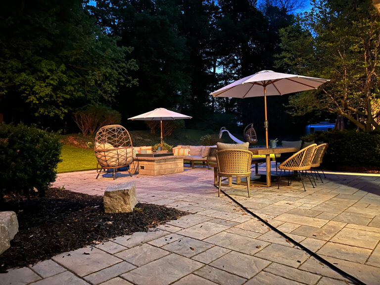 A paver patio with lounge chairs lit by low-voltage lights at night